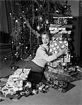 1950s WOMAN SITTING ON FLOOR IN FRONT OF XMAS TREE HOLDING PACKAGES