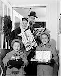 1960s FAMILY OF STANDING IN DOORWAY OF HOME WEARING WINTER COATS & HATS HOLDING WRAPPED GIFTS