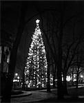 1950s TALL CHRISTMAS TREE LIT UP IN MIDDLE OF TOWN SQUARE