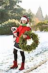 Woman in a park holding a Christmas wreath and a dog