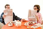 Couple having breakfast and reading newspaper together