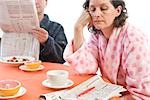 Tired woman with her husband at breakfast looking at classifieds