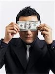 man holding up an American bill against his eyes