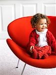 Little Girl in White and Red Outfit Sitting on a Red Chair in a White Room