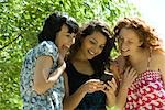 Three young women outdoors, looking at smartphone together