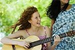 Young woman playing acoustic guitar outdoors, laughing