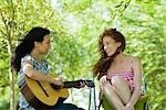 Two young women sitting outdoors, one playing acoustic guitar