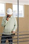 Construction supervisor at interior railing using walkie-talkie looking down