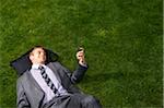 Businessman Lying on Grass Reading Text Message