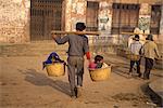 Taxi enfants, deux enfants transportés dans des paniers sur un poteau par un homme à Bhaktapur, Népal, Asie
