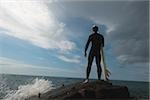 Homme debout sur le rocher avec planche de surf en regardant l'océan