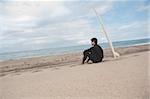 Junger Mann sitzt am Strand mit seinem Surfbrett