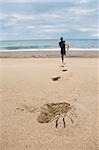 Mann läuft auf Sand Richtung Meer mit dem Ausscheiden aus seinen Spuren am Strand