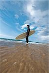 Young man standing with his surfboard near shoreline