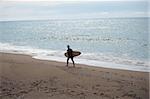 Junger Mann zu Fuß entlang der Küstenlinie mit seinem Surfbrett