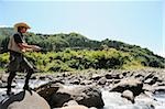 Man with straw hat standing on stone and holding fishing rod