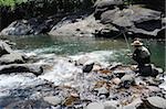 Man with straw hat sitting on stone and fishing