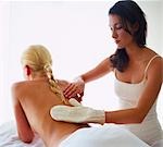 woman giving another woman a back massage with a massage glove