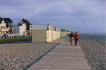 Couple walking along wooden planche (boardwalk), shingle beach, Cayeux sur Mer, Picardy, France, Europe