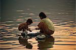Mother and child silhouetted at dusk, washing clothing in Phewa Tal River, Pokhara, Nepal, Asia