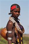 Lady Hamer, portant robe de peau de chèvre traditionnel décoré avec des coquilles de cowie, transportant kalash sur son chemin vers les marchés, Dombo village, Turmi, Omo basse vallée, Éthiopie, Afrique