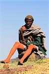 Pilgrim sitting on rock near church with mud on limbs which is thought to have magical healing properties, Lalibela, Ethiopia, Africa