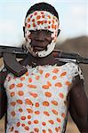 Kolcho village, Karo man with body painting, made from mixing animal pigments with clay, with kalashnikov slung over his shoulder, Lower Omo valley, Ethiopia, Africa