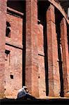 Old man wearing traditional gabi (white shawl) sitting in the sun reading holy bible, at monolithic church of Bet Medhane Alem (Saviour of the World), supported by 73 pillars, said to be largest rock hewn church in the world, Lalibela, World Heritage Site, Ethiopia, Africa