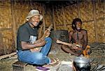 Dani men sit round fire, playing wooden guitar inside kitchen, South Beliam valley, Irian Jaya, Indonesia, Southeast Asia, Asia