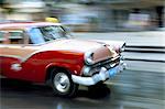 Panned shot of old American car splashing through puddle on Prado, Havana, Cuba, West Indies, Central America