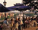 People at cafe tables in the open air at the Hanavsky Pavilion, with the river and the city of Prague behind, in The Czech Republic, Europe