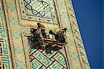 Workers in cradle refurbishing the 17th century Sher Dor Madressa, Registan Square, Samarkand, Uzbekistan, Central Asia, Asia