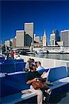 Homme lisant le journal et les passagers à bord du traversier de banlieue, avec Ferry Building et les toits du centre-ville de San Francisco dans le fond, Californie, États-Unis d'Amérique, Amérique du Nord