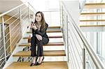 Businesswoman looking at cell phone on office staircase