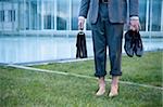 Businessman from waist down barefoot on grass outside of office building