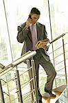 Businessman with financial newspaper on staircase talking on cell phone