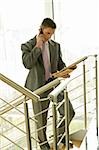 Businessman with financial newspaper on staircase talking on cell phone