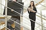 Businesswoman on staircase reading document and businessman walking down