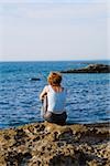 Rear view of a woman sitting on a rock, Baie de Biarritz, Biarritz, Pyrenees-Atlantiques, France