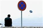 Rear view of a man sitting on a stone wall at the seaside, Baie De Cannes, Cote d'Azur, Cannes, Provence-Alpes-Cote D'Azur, France