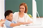 Side profile of a schoolboy with his teacher in front of a computer