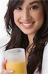 Portrait d'une jeune femme tenant un verre de jus d'orange et souriant