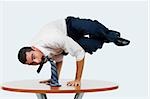 Portrait of a businessman doing a handstand on a table with a mobile phone in his mouth
