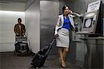 Businesswoman talking on a pay phone with a businessman standing behind her at an airport