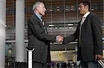 Side profile of two businessmen shaking hands at an airport lounge