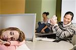 Young woman napping on a desk with a young man smiling in the background