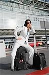 Businesswoman sitting on a suitcase and waiting for a taxi outside an airport