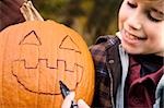 Boy drawing a human face on a pumpkin