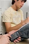 Close-up of a person's hand using a calculator and a young man sitting beside him