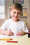 Portrait of a boy drawing on a sheet of paper and smiling